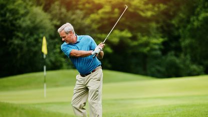 An older man hits a golf ball on the golf course.