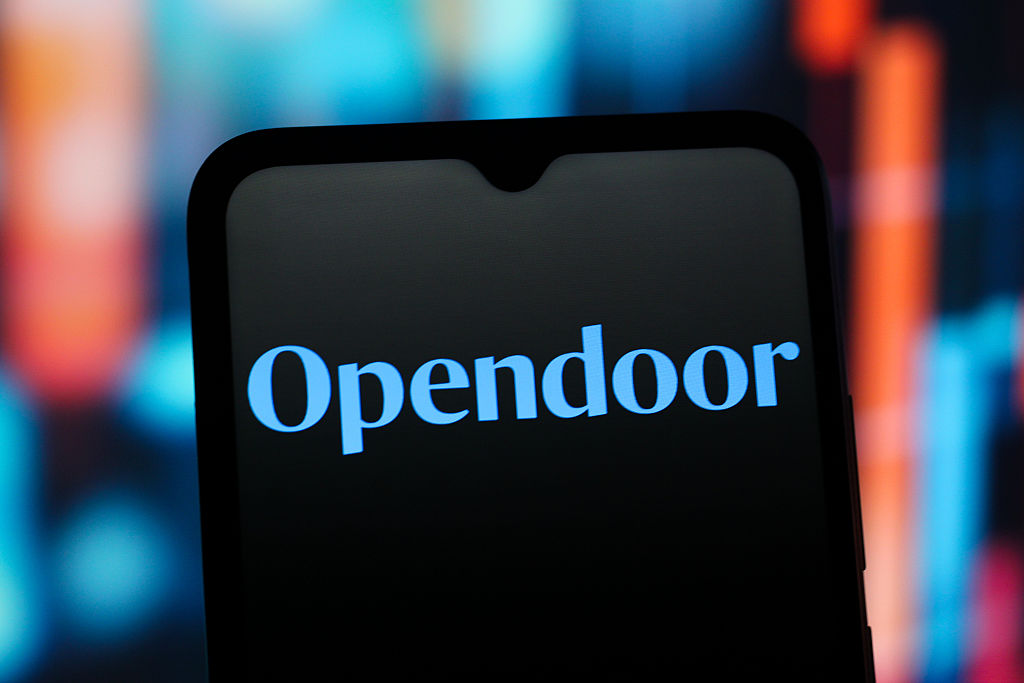 Opendoor Technologies logo on a smartphone with blurred red and blue lights in the background