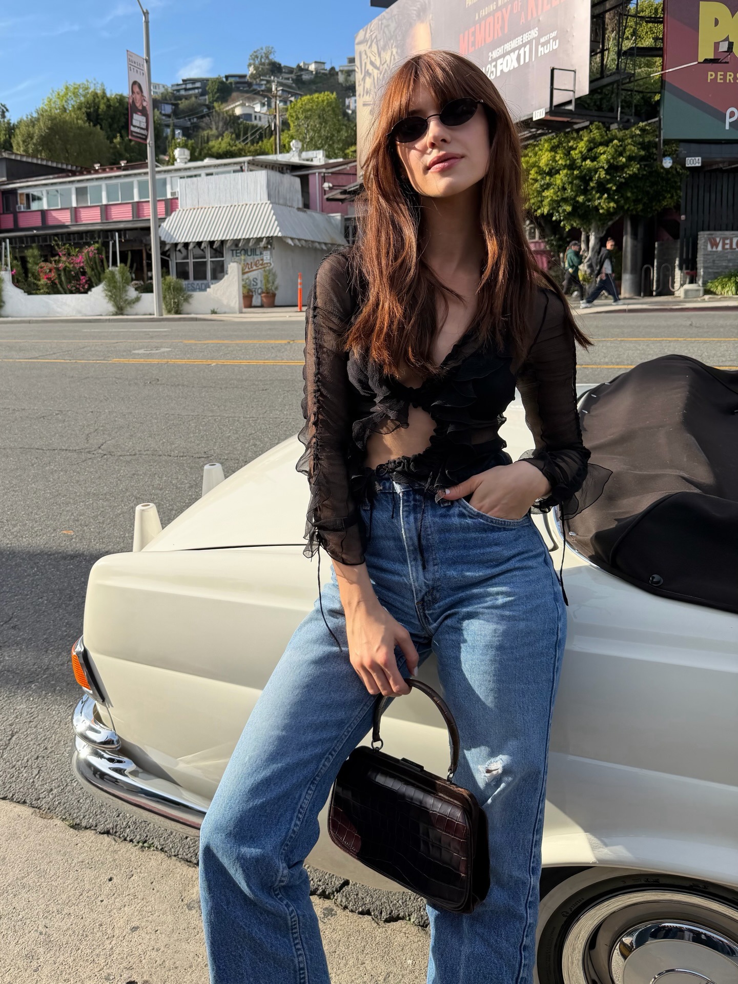 Daisy Edgar-Jones wearing a black going-out top with high-waisted jeans and a black vintage clasp bag on Sunset Boulevard in Los Angeles.