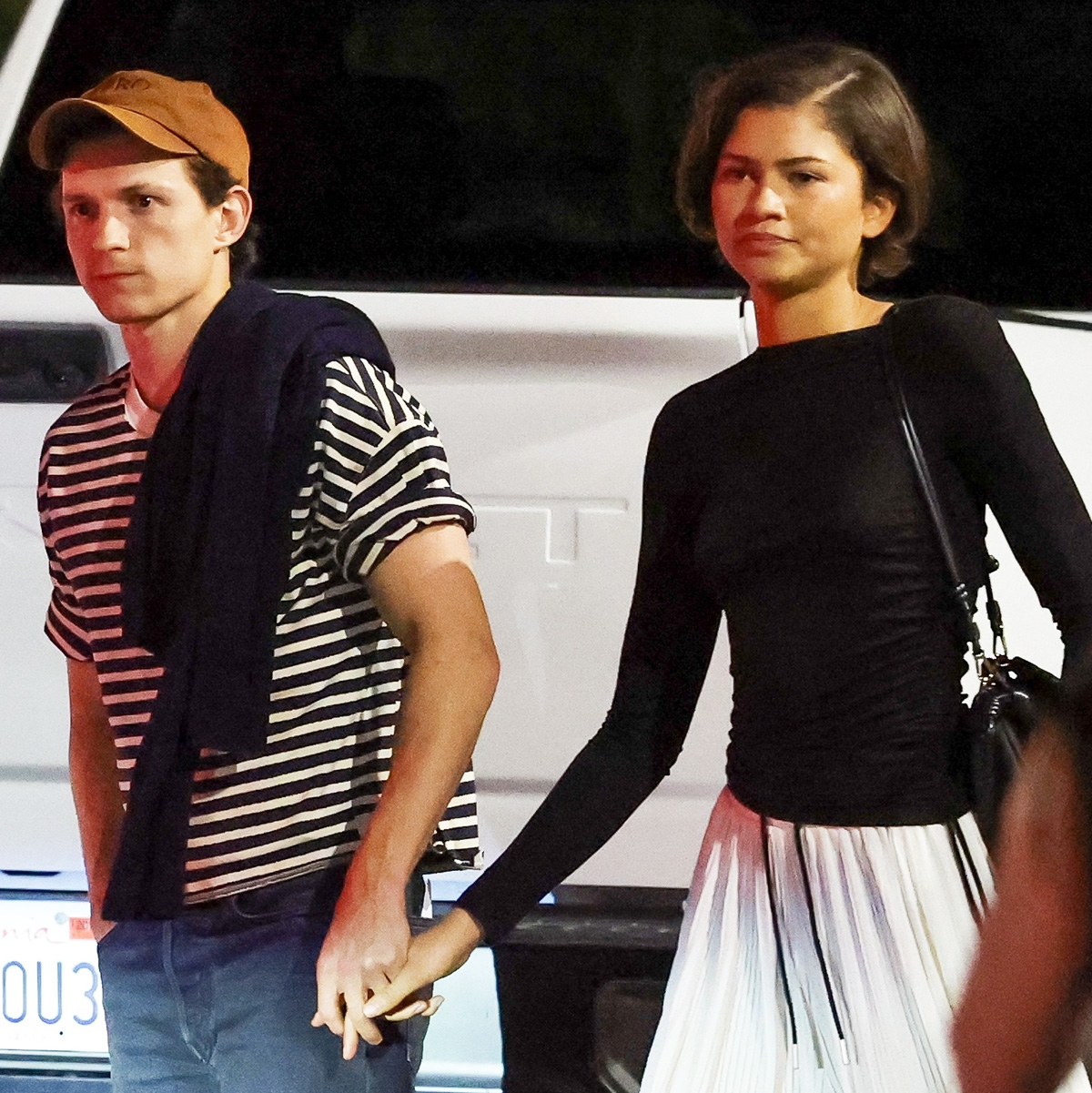 Tom Holland with Zendaya wearing a black top, white billowy pants, and black shoes