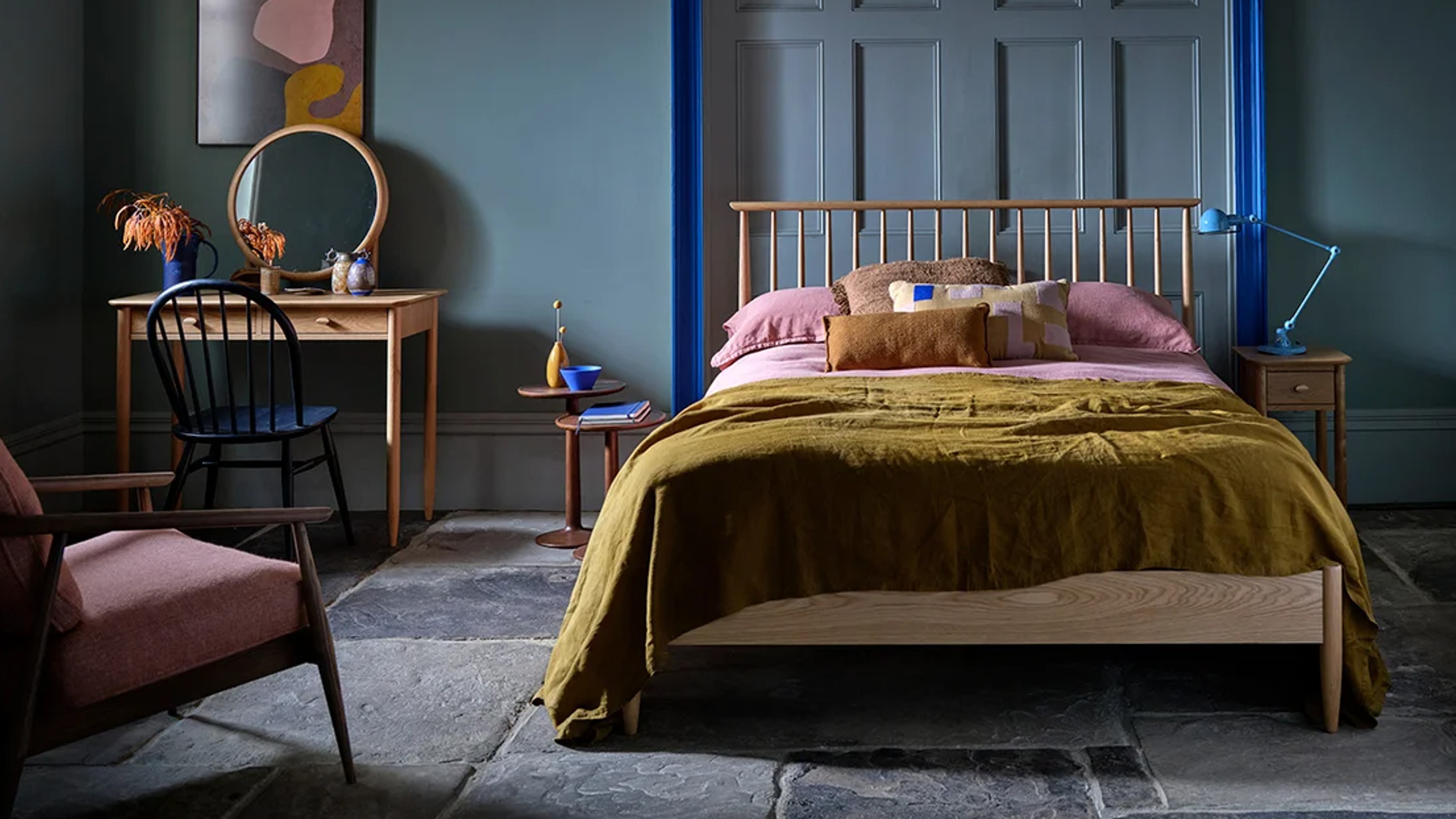 A dark bedroom with wooden Ercol bed frame and dressing table