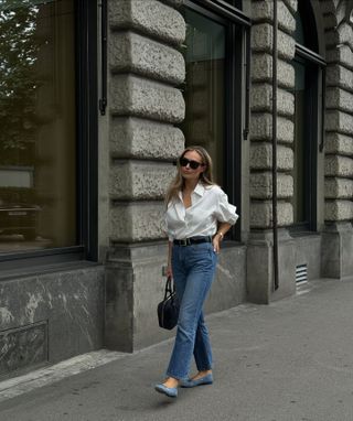 fashion influencer @oliviafaeh wearing a white button-down shirt, blue jeans, blue ballet flats, and a black nylon Prada bag