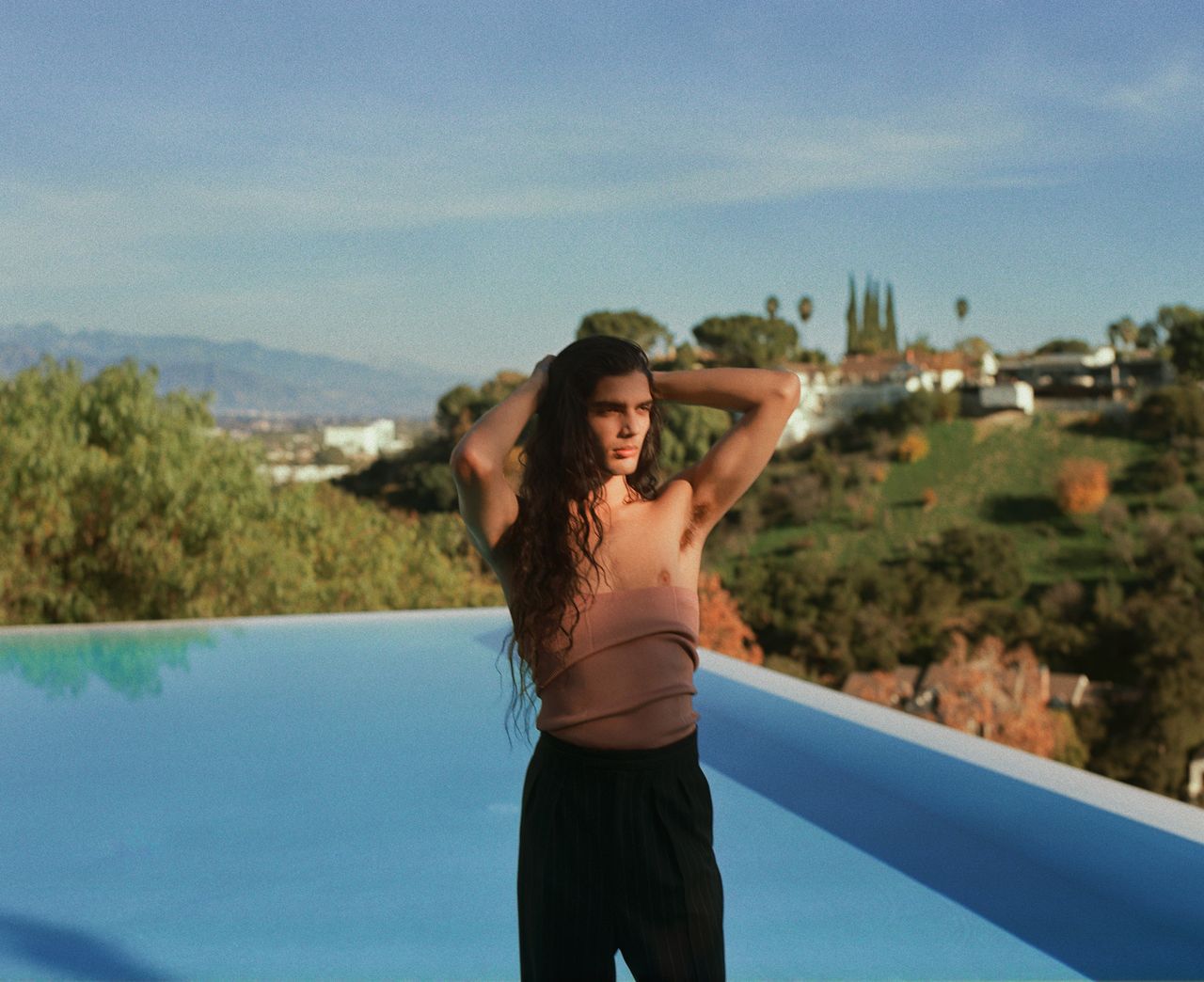 Man stood by pool in Dries van Noten menswear bustier top with Californian landscape behind