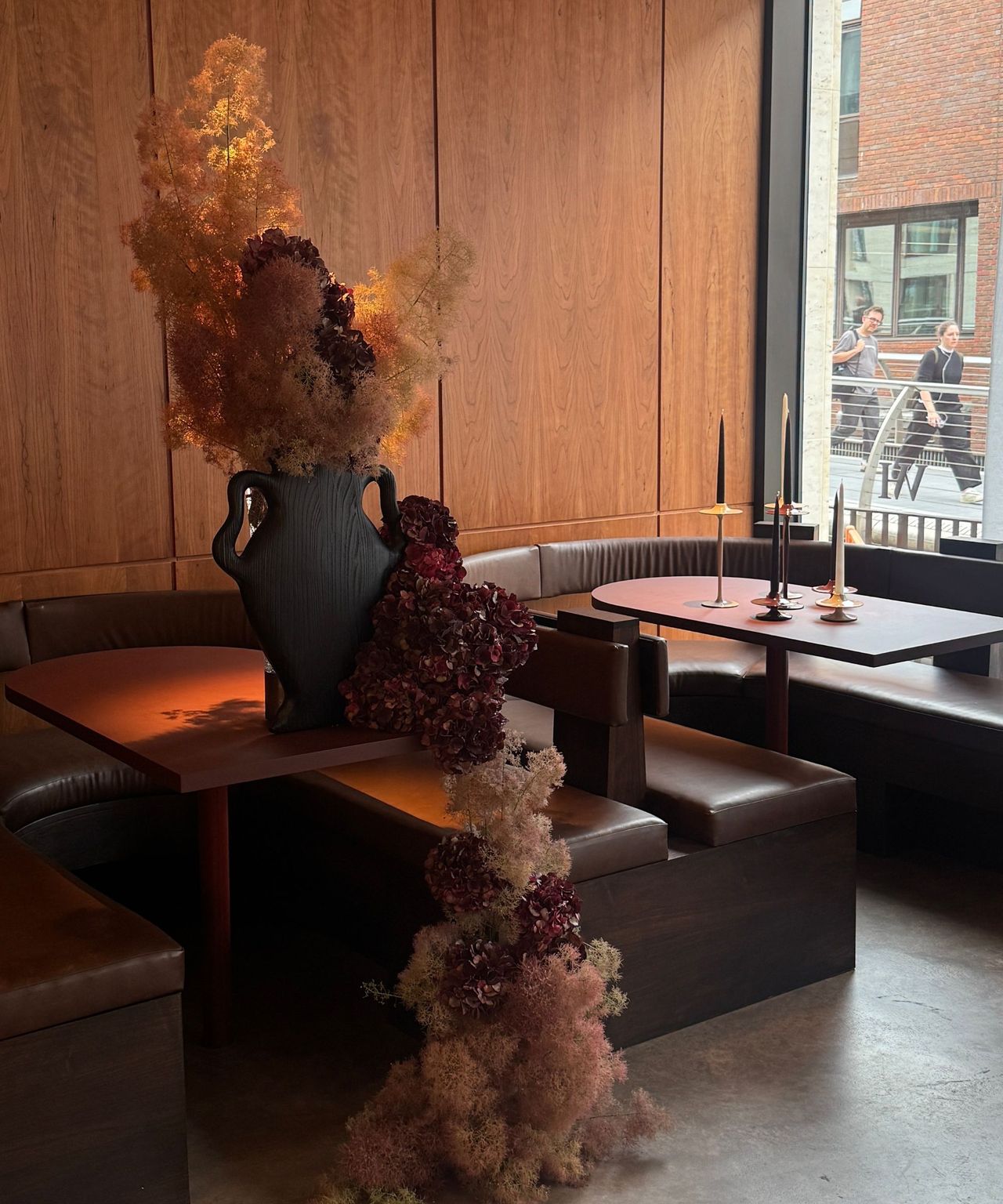 cafe with timber panelling, polished concrete floors, banquette seating, a timber vase and floral display draping down to the ground