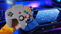 Hand holding grey N64 controller next to image of Hyperkin Mega95 handheld.