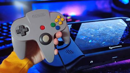 Hand holding grey N64 controller next to image of Hyperkin Mega95 handheld.