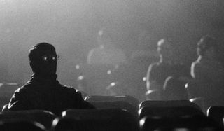 A man sitting in a dark theater, with light reflecting from his glasses