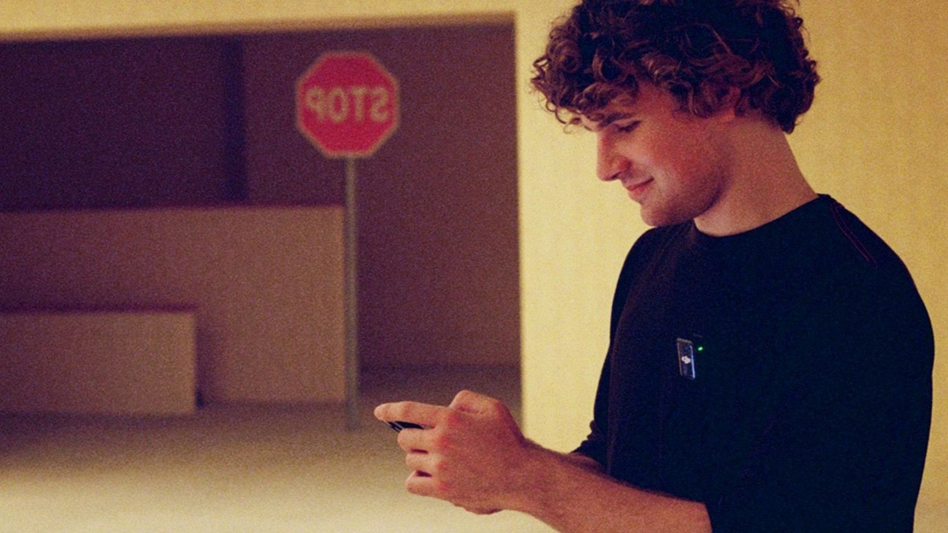 Kane Parsons on set of Backrooms, with a reversed stop sign in the background, a delicious foil for the headline which says he is not stopping making Backrooms stuff