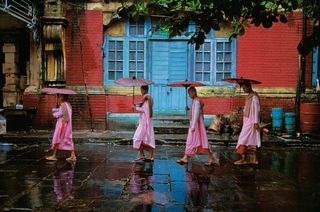’Procession of Nuns’, Rangoon, Burma, by Steve McCurry, 1994. Nuns with pink robes and umbrella's walking down a street.
