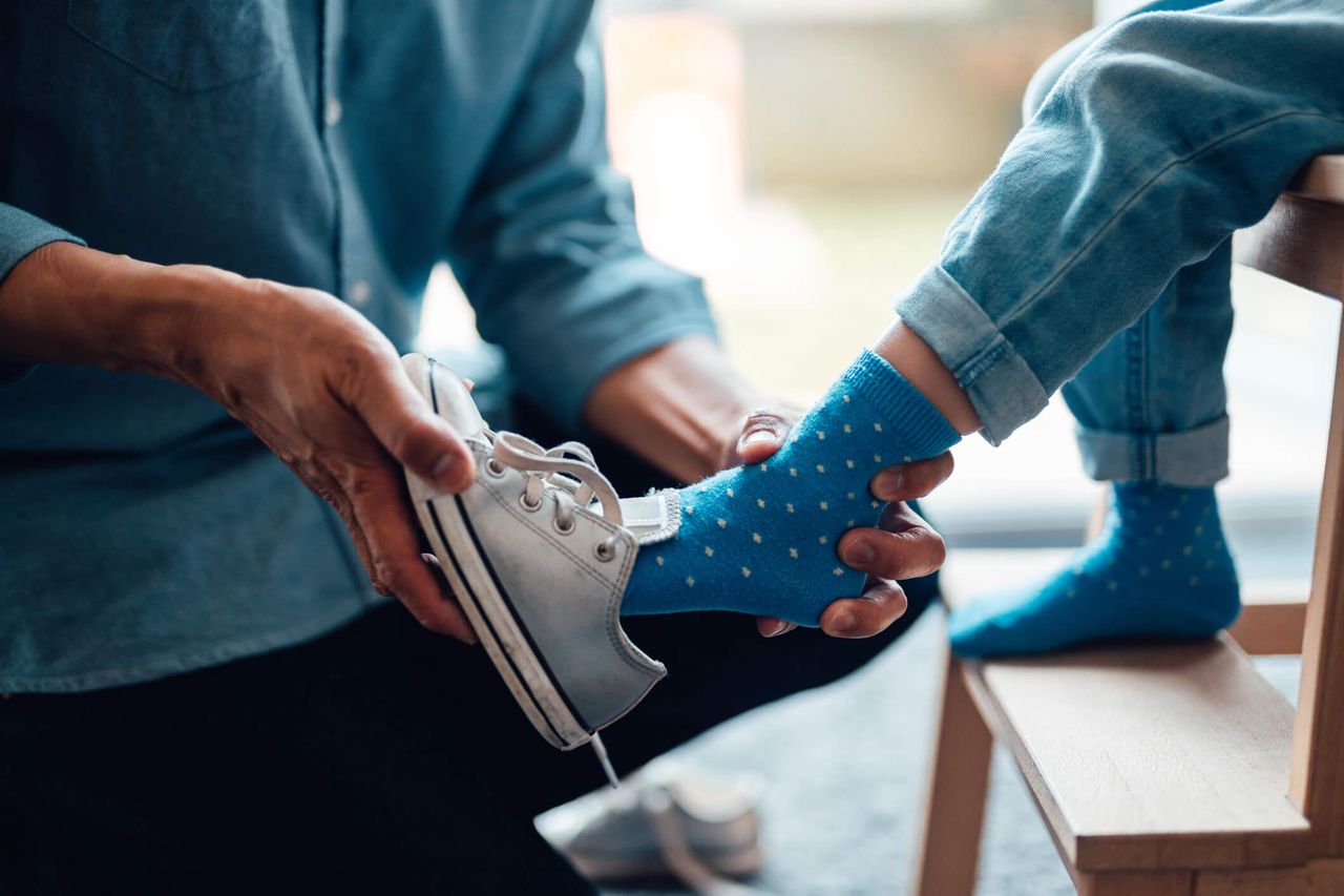 A parent putting on their child&#039;s shoes for them.