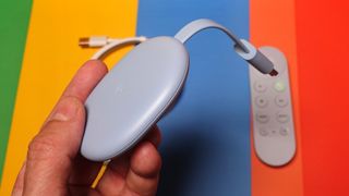 The Chromecast with Google TV with remote and power cable in the background, is one of the best streaming devices for its value