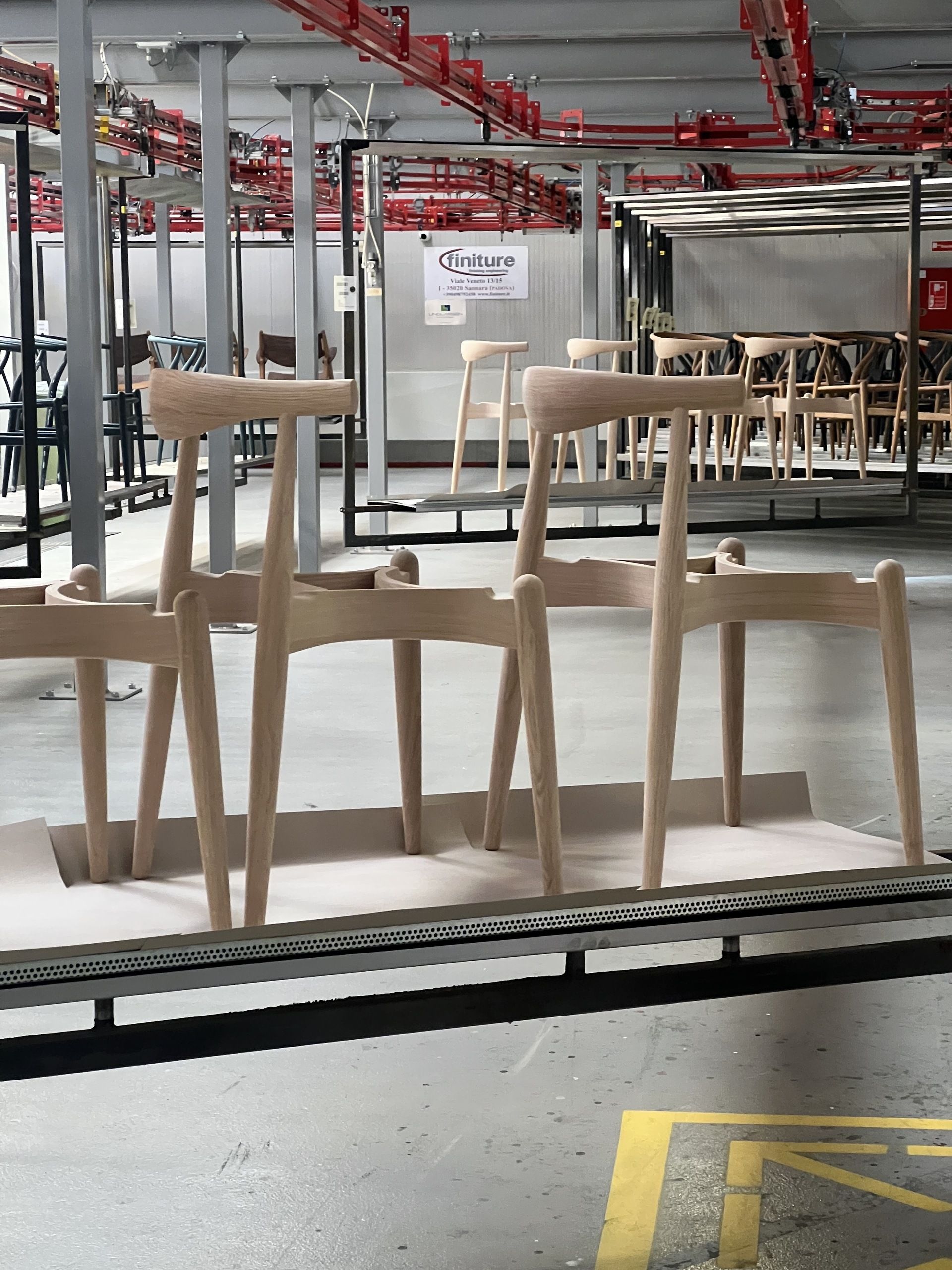 Image of a factory with lots of chairs around. There are three wishbone chairs on an elevated metal rack.