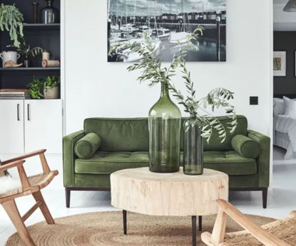 A white living room with a green sofa and natural wood chairs 