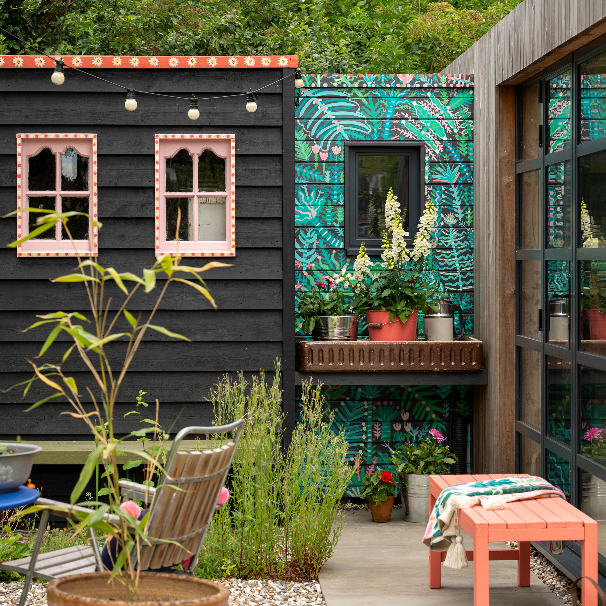 a black shed beside a garden building that has been painted with a decorative flower print