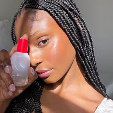 A model holding a bottle of Glossier You by their face