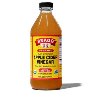 A glass bottle of Bragg Organic Apple Cider Vinegar With the Mother with yellow and red label, with black text and black lid