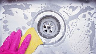 A stainless steel sink being cleaned with soap and a sponge