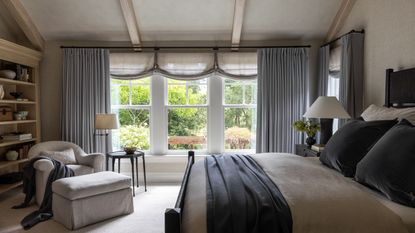 neutral bedroom with gray curtains, taupe bedding with dark blue throw and cushions
