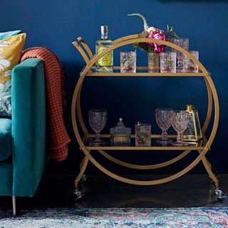 Asda gold drinks trolley with glasses against a dark blue wall