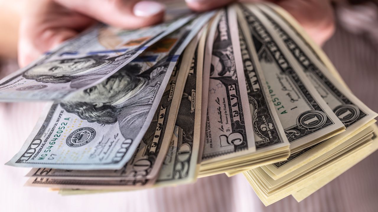 Several five- and one-dollar bills are fanned out in a woman&#039;s hand.