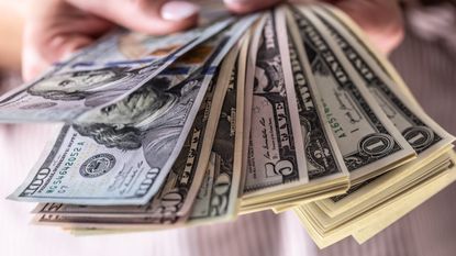 Several five- and one-dollar bills are fanned out in a woman's hand.