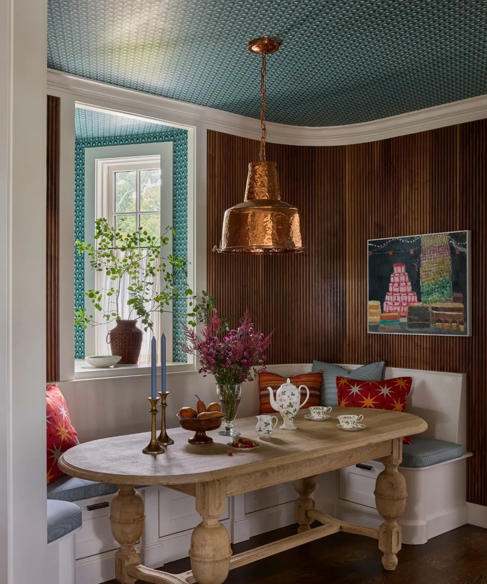 a dining nook with a white built in bench, a large table, wood walls, and a teal wallpapered ceiling