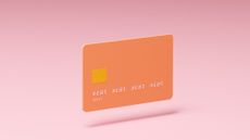 Conceptual image of an orange credit card with letters spelling "debt" instead of account numbers hovering above a pink background