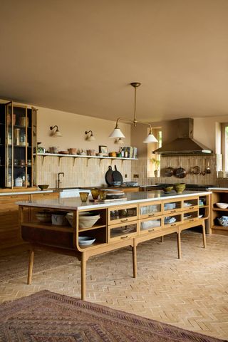 An oak multifunctional kitchen island with glass drawers and a marble island worktop. Above at shaded pendant lights