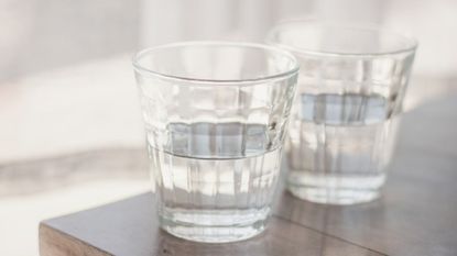 Two clear drinking glassed filled with water on a table