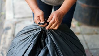 person tying together a black bin/trash bag