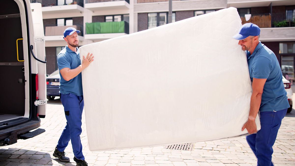 Two men hold a new mattress as they carry it from a van to a home, ready for delivery