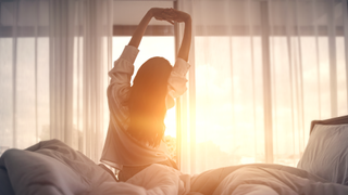 Woman stretching on bed in front of open curtains