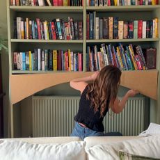 Woman adding plywood arch to bottom of green bookshelf above radiator