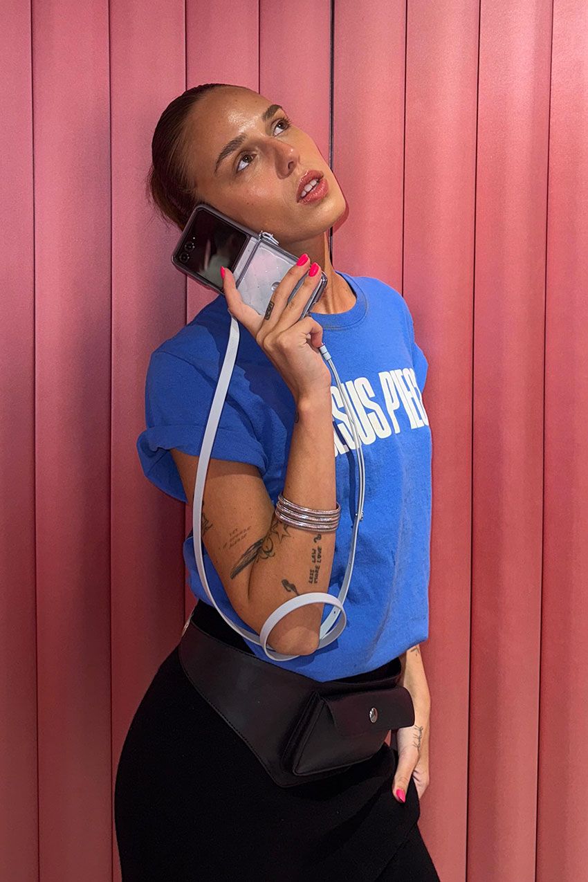 A woman wearing a blue graphic T-shirt, a black leather utility belt, and a black skirt.