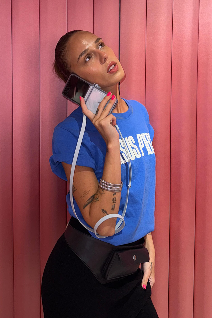 A woman wearing a blue graphic T-shirt, a black leather utility belt, and a black skirt.