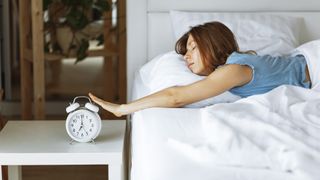 A woman reaches out of bed to turn her alarm clock off in the morning