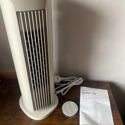 The small Meaco Sefte Tower Fan sitting on a sideboard next to the instruction manual and remote control in a taupe room