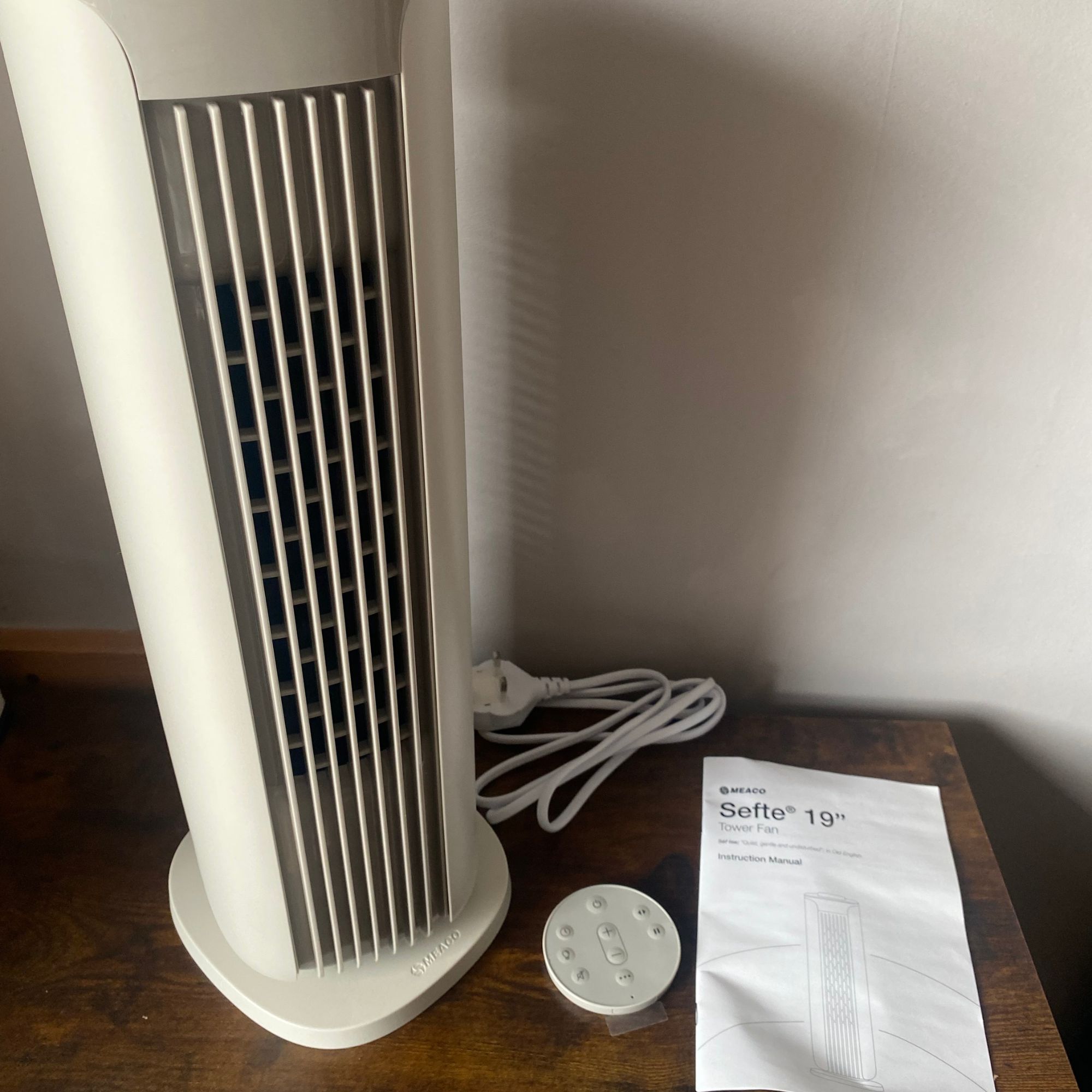 The small Meaco Sefte Tower Fan sitting on a sideboard next to the instruction manual and remote control in a taupe room
