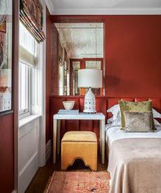 A colorful bedroom with deep red walls, yellow stool and neutral bedding