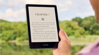 A Kindle being read outside in front of a big green space