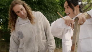 Meghan Markle wearing a beekeeper suit scraping honey off a tray next to a man in a white beekeeper outfit