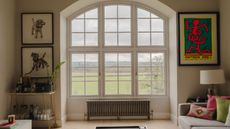 A small baseboard radiator, mounted under a very large arched window in a living room, overlooking green fields. 