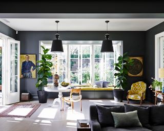 A living room painted in dark gray, with mustard accents and large light windows.