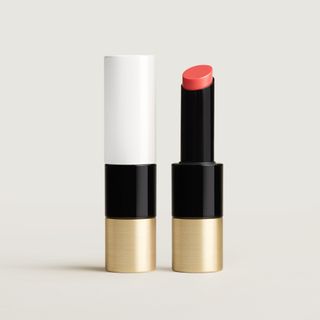 Hermès pink tinted lip balm in a black and gold case on a white background