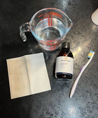 A glass jug filled with water, a bottle of glycerin, an old toothbrush, and a white cloth