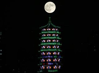 a tall temple structure with a large fully illuminated moon above.