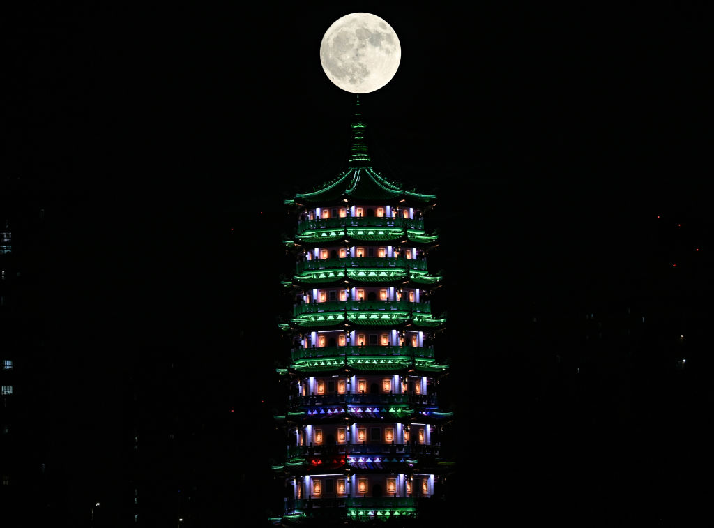 Una estructura de templo alta con una luna grande y completamente iluminada en la parte superior.