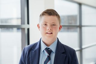Headshot of smiling down syndrome teenage boy in corridor at school.