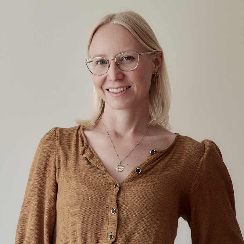 A headshot of a woman with blonde hair and glasses smiling at the camera