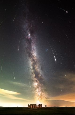 stone arrangements are at the base of the image and the milky way stretches vertically though the sky above while perseid meteors appear to rain down through the sky as long streaks of light.